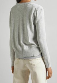 Pull gris en maille avec ourlet et poignets côtelés, présentant un col rond et une texture douce, associé à un jean beige clair.