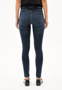 Tunna mörkblå jeans med hög midja, synliga sömmar, två bakfickor och en subtil textur. Bärs med svarta skor.