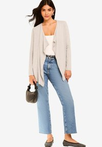 Cardigan grigio chiaro aperto sopra una maglietta bianca, abbinato a jeans blu a vita alta. Ballerine nere con borchie e una piccola borsa nera completano il look.