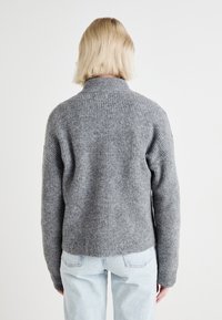 Szary sweter dzianinowy z wysokim kołnierzem, prążkowaną fakturą i skróconym dołem. Nosi się go z jasnoniebieskimi, lekko luźnymi dżinsami.