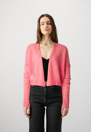 Cardigan corto rosa realizzato in tessuto morbido, con maniche lunghe e scollatura a V, abbinato a jeans neri a vita alta.