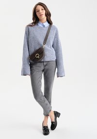 Niebieski sweter robiony na druty, szare dżinsy i czarne mokasyny na obcasie. Całość dopełnia mała brązowa torba na ramię z złotym akcentem.