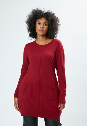 Tunic rosso a maglia con scollatura rotonda, maniche lunghe, polsini a coste e due tasche frontali caratterizzate da una texture a coste verticale.