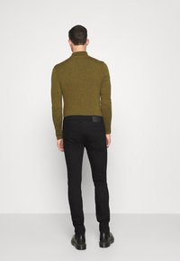 Olivgrön, åtsittande tröja med långa ärmar, strukturerad tyg och hög krage, i kombination med svarta slim fit byxor och svarta stövlar.