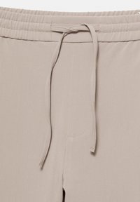 Pantalons de survêtement doux, beiges, avec une taille élastique et un cordon de serrage. Présente des poches latérales et une texture lisse.