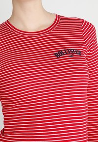 Röd- och vitrandig långärmad tröja med rund halsringning, med en svart "Hollister"-logotyp på bröstet. Slät bomullstyg.