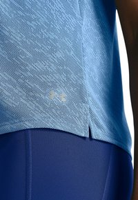 Helles blaues Sportshirt mit strukturiertem Muster, seitlichem Schlitz und silbernem Logo. Kombiniert mit dunkelblauen Leggings, die ein figurbetontes Design zeigen.