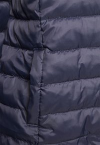 Marineblaue gesteppte Jacke mit gesteppter Struktur, glattem synthetischem Stoff und tonalem Steppnähten, entworfen für Isolierung und Komfort.
