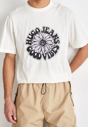T-shirt en coton blanc avec un motif graphique représentant une fleur violette et le texte "HUGO JEANS GOOD VIBES". Manches courtes, coupe décontractée.