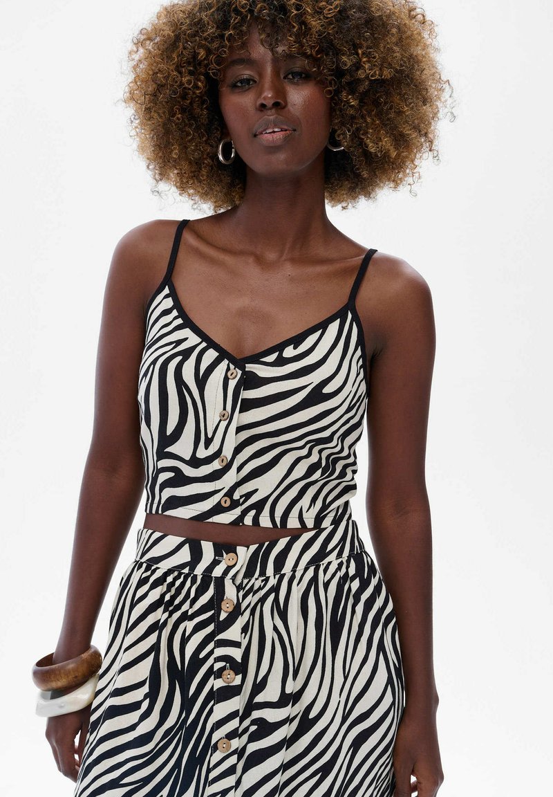 Czarnobiała, w paski zebra, krótka bluzka z dekoltem w serek, zapinana na guziki, na cienkich ramiączkach, w zestawie z dopasowaną spódnicą o podobnym wzorze.