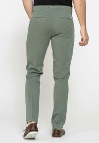 Pantaloni slim-fit da uomo in cotone verde oliva. Caratterizzati da tasche posteriori con bottoni e orli cuffati, abbinati a scarpe casual marroni.