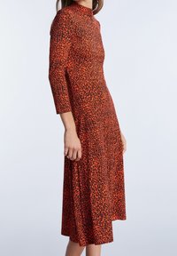 Punainen mekko mustalla leopardikuvioinnilla, korkea kaula-aukko, kolmi neljänneksen hihat, A-linjainen siluetti, pehmeä tekstuuri ja keskikorkea pituus.
