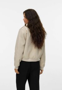 Felpa beige con polsini e orlo a costine, caratterizzata da un fit rilassato e una texture morbida. Indossata con pantaloni neri, vista da dietro.