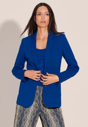 Blue fitted blazer with a notched lapel, two buttons, and front pockets. Paired with patterned trousers. Smooth fabric texture.