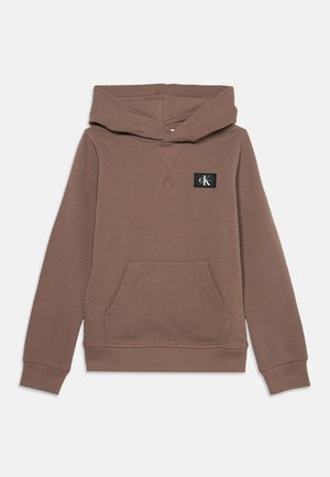 Sweat à capuche marron avec poche avant et petit patch logo noir sur la poitrine gauche, présenté sur fond blanc.