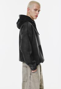 Felpa nera con cappuccio, dotata di cordino e tasca frontale, abbinata a pantaloni beige chiaro a vestibilità ampia con grandi tasche laterali.