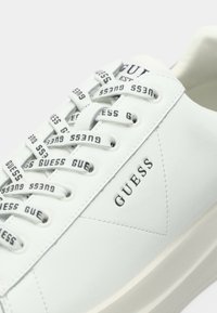 Fehér GUESS sneaker, márkázott fűzőkkel és a oldalán, valamint a nyelvén dombornyomott logóval, tiszta varratokkal és vastag talppal.