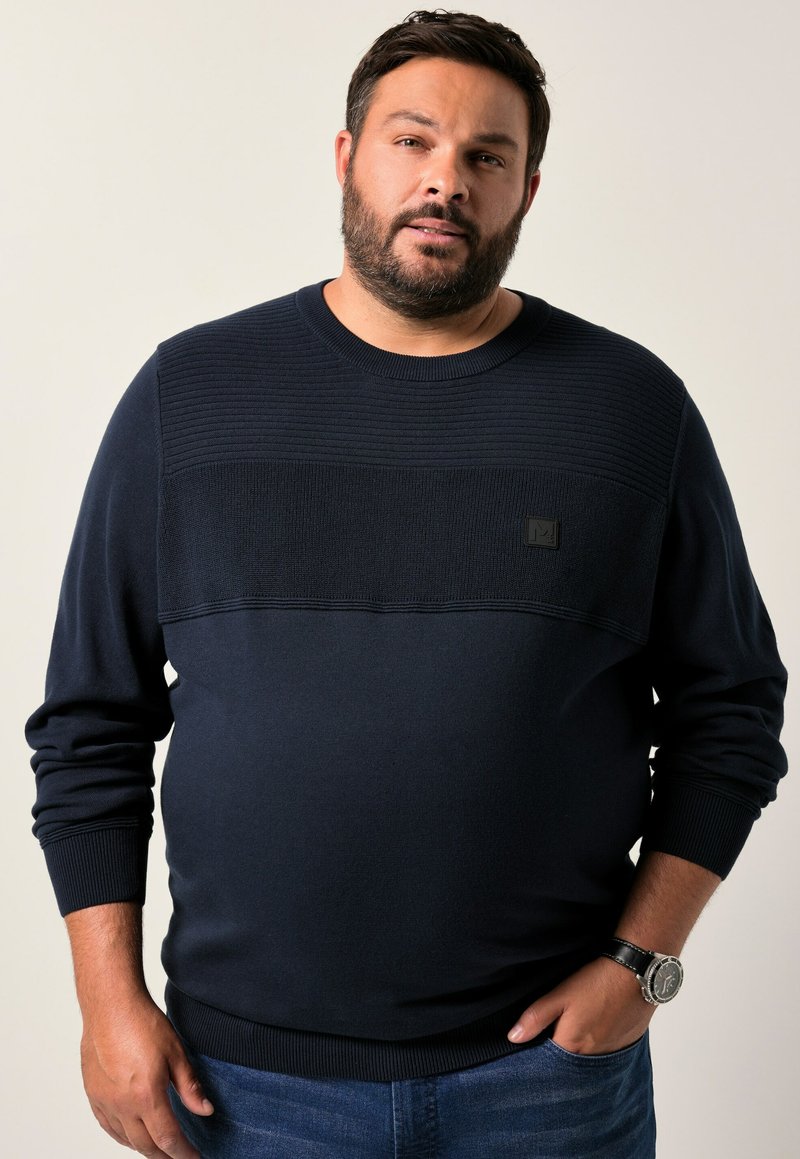 Dunkelblauer Pullover mit strukturiertem Rippstrick im oberen Bereich und solidem unteren Teil. Mit kleinem Logo auf der Brust und gerippten Bündchen.