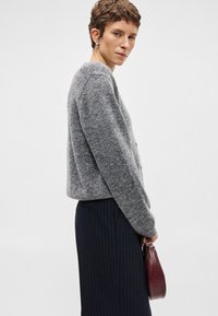 Grijze wollen cardigan met een relaxte pasvorm, knoopsluiting en geribde manchetten. Gecombineerd met gestreepte broek en een kleine, textuurrijke bordeauxrode handtas.