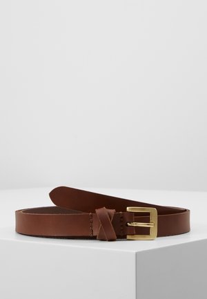 Brunt læderbælte med gyldent rektangulært spænde, rullet sammen på en hvid overflade mod en ensartet lys grå baggrund.