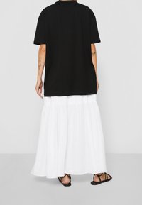Černé oversize tričko vyrobené z bavlny, spárované s volnou bílou maxi sukni s vrstveným designem. Sandály dotvářejí outfit.