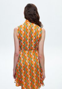 Vestido sin mangas en un patrón geométrico de color naranja, verde y melocotón. Tejido ligero con una cintura ajustada, que fluye suavemente hasta por encima de la rodilla.