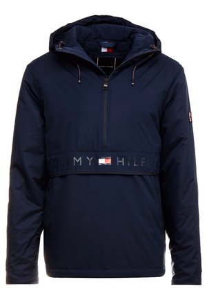 Navy blauwe jas met capuchon en ritssluiting aan de voorkant, "Tommy Hilfiger" tekst en vlaglogo op de borst, en vlagpatch op de linker mouw.
