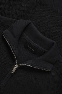 Pulover negru cu fermoar, cu design tricotat texturat. Prezintă un guler înalt și fermoar argintiu. Etichetă vizibilă în interiorul gulerului.