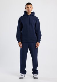 Sudadera azul marino y pantalones de chándal a juego, hechos de un tejido suave. Cuenta con un bolsillo frontal y una capucha ajustable con cordones. Ajuste casual.