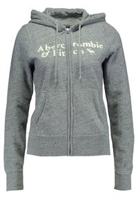 Šedá mikina na zip z měkké látky, má klokánčí kapsu, kapuci se stahovací šňůrkou a bílý textový logo na přední straně.