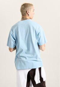 Světle modré bavlněné tričko s krátkým rukávem a pohodlným střihem, s jednoduchým designem a prošitým lemem, zv view z zadní strany.
