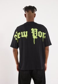 Tricou din bumbac negru, cu un text verde, mare și picurând, care scrie "New York" pe spate. Mâneci scurte și design lejer.