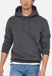 Gray cotton hoodie with a front pocket, adjustable drawstring hood, ribbed cuffs, and a relaxed fit, layered over a white shirt.
