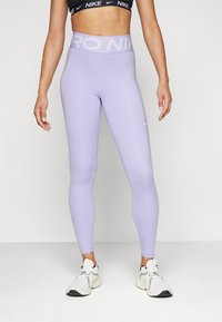 Leggings de culoare mov deschis, cu talie înaltă, care prezintă textul „PRO NIKE”. Realizate dintr-un material elastic și neted, asortate cu adidași albi.