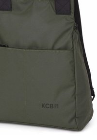 Bolsa tote de color verde oscuro con bolsillo frontal, correa negra y logo "KCB Vegan Bags" en la esquina inferior derecha.