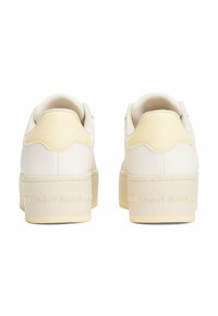 Baskets plateforme blanches en cuir texturé avec semelles en caoutchouc. L'arrière présente un design ondulé avec la marque "TOMMY JEANS" embossée dans le talon.