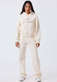 Sudadera con cremallera de color crema con el logo bordado "PXP", combinada con pantalones de chándal a juego, confeccionada en un suave tejido texturizado.