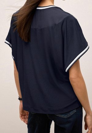 Tmavě modrý krátký rukáv top s kulatým výstřihem, s bílým lemem na rukávech. Měkká tkanina s uvolněným střihem a hladkou texturou.