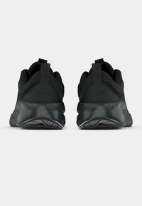 Un pătrat de adidași negri Nike văzuți din spate, având talpă groasă și curele de prindere pe un fundal simplu deschis.