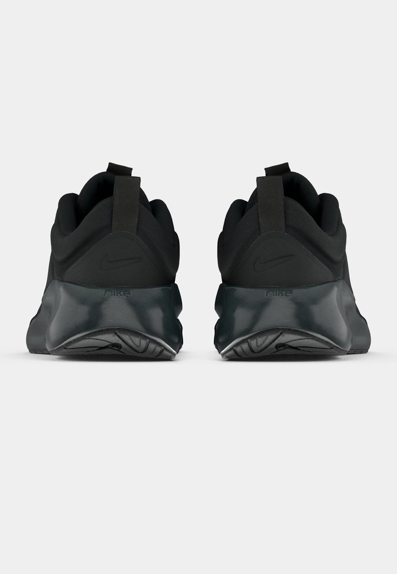 Par de zapatillas negras de Nike mostradas desde atrás, con suelas gruesas y tiradores, sobre un fondo claro liso.