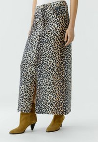 Leopardmuster-Midi-Rock in Beige und Schwarz, mit einem seitlichen Schlitz, jeansähnlicher Textur und klassischem Five-Pocket-Design. Kombiniert mit olivgrünen Ankle Boots.