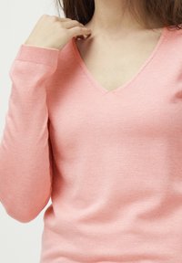 Pull-over en v léger rose en tricot doux avec des poignets côtelés. Présente une coupe ajustée, une texture subtile et des coutures minimales.
