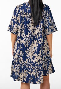 Robe bleu marine avec motif floral beige, manches courtes et ourlet à volants en étages. Tissu lisse et coupe décontractée. Vue de dos.