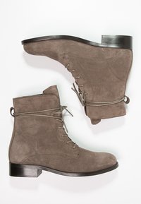 Braune Wildleder-Stiefeletten mit runder Zehenform, Schnürdesign und einem niedrigen schwarzen Absatz. Glatte Oberfläche mit minimalen Nahtdetails.