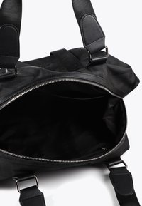 Svart väska med öppen dragkedja och rymligt inre, försedd med robusta remmar och en stilren, minimalistisk design.