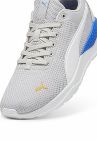 Hellgraue Mesh-Sneaker mit weißen und blauen Akzenten, featuring ein gelbes Logo, strukturierte Oberfläche und eine gepolsterte weiße Sohle.