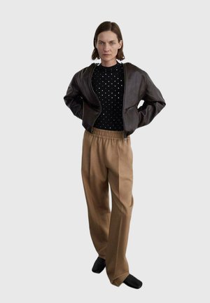 Veste bomber en cuir marron sur un pull noir à pois, assortie avec un pantalon large beige et des chaussures noires.