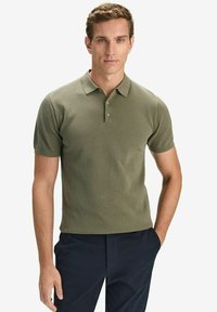 Olivi vihreä lyhythihainen polo-paita, jossa on tekstuuri, kauluspäällä ja kolmella napilla varustettu nappisulku, yhdistettynä tummiin housuihin.