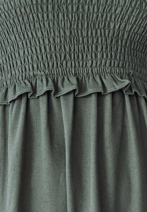 Robe en tissu vert avec un corsage smocké et une bordure froncée, dotée d'une texture douce et d'une jupe fluide. Le motif est uni sans accents supplémentaires.