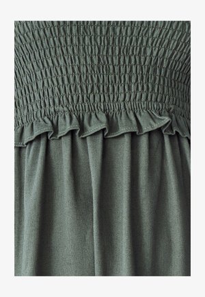 Robe en tissu vert avec un corsage smocké et une bordure froncée, dotée d'une texture douce et d'une jupe fluide. Le motif est uni sans accents supplémentaires.